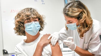 En ung person i munskydd vaccineras mot covid-19 av en sjukskötare i munskydd.