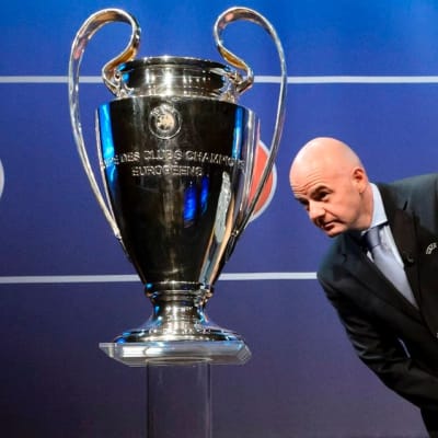 UEFA:n pääsihteeri Gianni Infantino kurkistelee Mestarien liigan pokaalin vieressä.