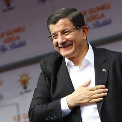 Hymyilevä Ahmet Davutoğlu käsi sydämellä. 
