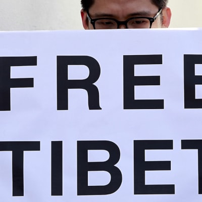 Silmälasipäinen mies pitelee edessään Free Tibet -kylttiä.
