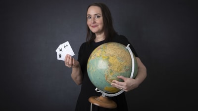 kvinna håller en jordglob med ena handen och med denandra handen visar hon kort med symboler för flyg, tåg eller båt