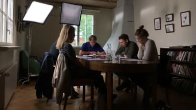 Regissören Claes Olsson och skådespelare sitter runt ett bord för manusgenomgång.