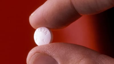 en tablett aspirin mellan tumme och pekfinger
