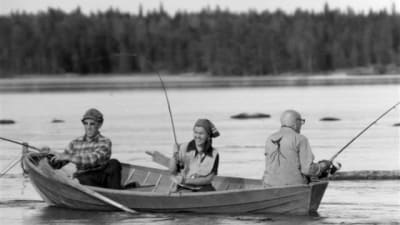 Gammal svartvit bild på en roddbåt och tre personen som sitter i båten och fiskar.