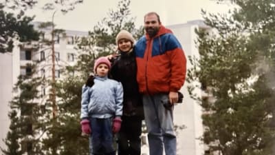 Anna Soudakova äidin ja isän kanssa Turun Lausteella 1991. Perhe on juuri muuttanut Leningradista Suomeen. Seisovat männikköisellä kalliolla, taustalla kerrostaloja.