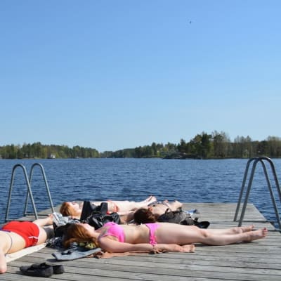 Nuoria naisia ottamassa aurinkoa uimarannan laiturilla.