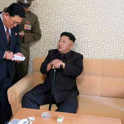 Kim Jong-un istuu sohvalla kävelykepin kanssa, seurue kirjoittaa lehtiöihinsä