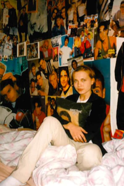 Ett foto från 90-talet där Lisa Ahlvik sitter i sin säng omgiven av affischer.