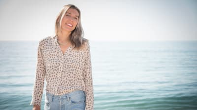 Kvinna står på en strand och ler mot kameran.