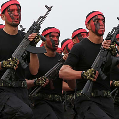 Joukko Hamasin taistelijoita marssii rynnäkkökiväärit käsissään, kasvot maalattuina punaiselle ja mustalla värillä, otsallaan punainen panta.