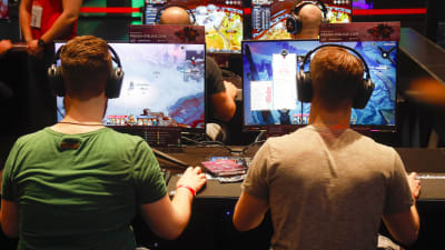 Två män sitter framför varsin dataskärm och spelar. Männen sitter med ryggen mot kameran
