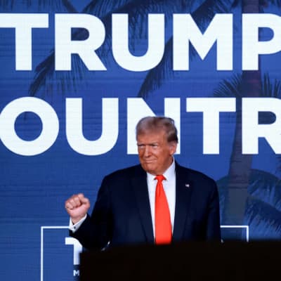 Donald Trump står framför en blå bakgrund med texten "Trump country". 