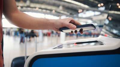 En person håller i en smarttelefon med skärmen neråt mot en läsare på en flygplats.