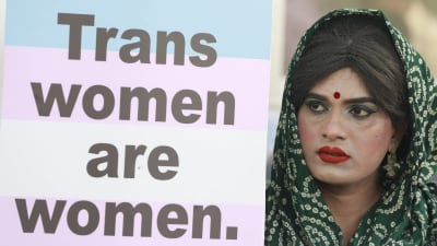 En sminkad demonstrant i huvudduk med med en skylt med texten "Trans women are women", alltså "Transkvinnor är kvinnor".