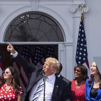 Trump on kuvassa lehdistötilaisuudessa. Hän osoittaa oikealla kädellään kohti taivasta. 