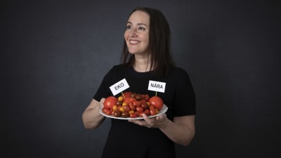 kvinna håller en tallrik med tomater i sin hand med skyltarna EKO och NÄRA