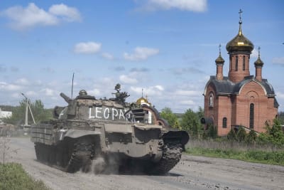 Ukrainska arméns stridsvagn kör förbi ett kapell med lökkupoler på taket. På stridsvagnens övre del har någon skrivt "Leopard" i vit färg.