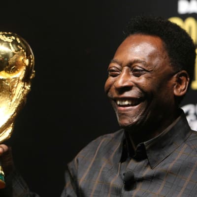Brasilian legenda Pelé pitelee MM-kisojen pokaalia hymyillen kädessään.