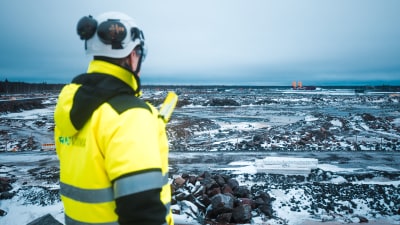 En man i arbetskläder och hjälm tittar ut över det kala området i Hanhikivi där kärnkraftverket ska byggas.