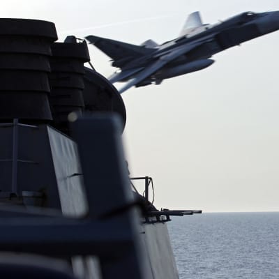 Venäläinen lentokone syöksyy kuvan vasemmassa reunassa olevan aluksen ohi. Kuva on otettu yhdysvaltalaisen sotilasaluksen kannelta.