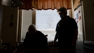 Anonym bild på en äldre och en hemvårdare. Siluetterna syns mot ett fönster.