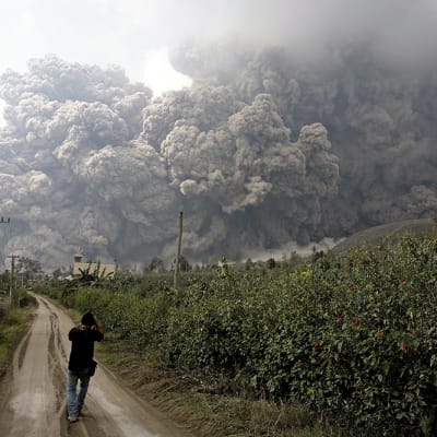 Mustapaitainen mies ottaa valokuvaa massiivisesta tulivuorenpurkauksesta.