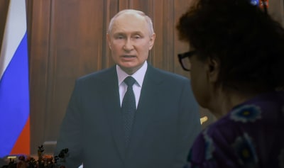 Vladimir Putin håller tal på tv, en äldre kvinna tittar på.