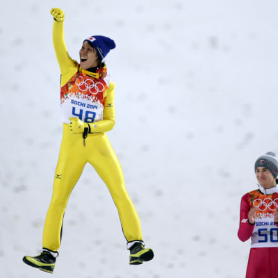 Japanin Noriaki Kasai hyppää ilmaan palkintoseremoniassa. Puolan Kamil Stoch antaa aplodit.