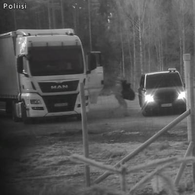 En person förflyttar sig från en lastbil till en bil. Personen håller i ett stort föremål.