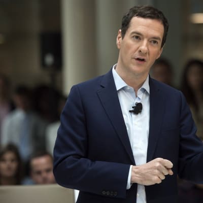 Osborne puhuu viittilöiden käsillään. Hänellä on tummansininen puku ja kauluspaita ilman kravattia. Mikrofoni on kiinnitetty hänen paitaansa. Taustalla näkyy yleisöä.