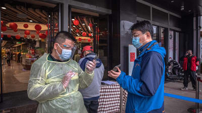 En kontrollant kollar via en mobilapplikation hälsotillståndet hos en man i ett köpcenter i Wuhan 31.3.2020.