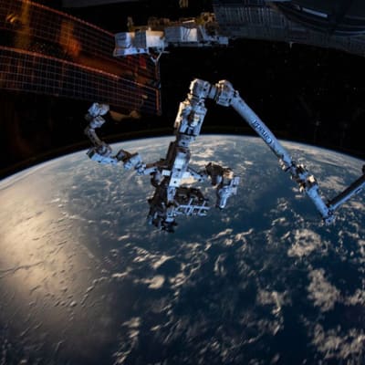 Moninivelinen roborttivarsi, taustalla ISS:n aurinkopaneeli  ja maapallon kaareutuva pinta. 