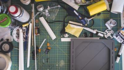 Ett arbetsbord med en mängd små verktyg, penslar, färger och lim.