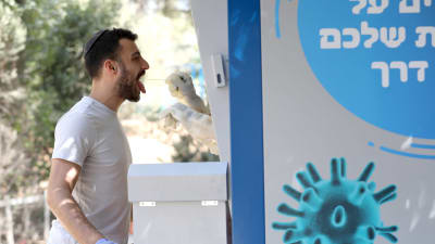 En israelisk man gapar medans någon gör ett coronatest på honom från en kioskliknande testpunkt.