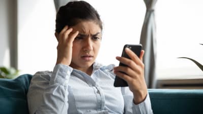 En bekymrad kvinna tittar på sin telefon.