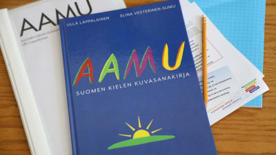 Kuvassa on suomen kielen kuvasanakirja ja vihko sekä kynä.