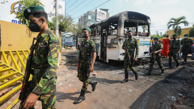 Soldater i munskydd går förbi en nedbränd buss.