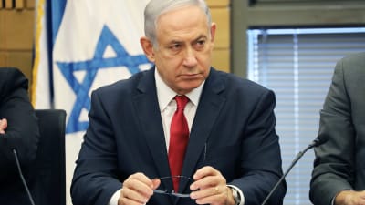 Benjamin Netanjahu ser fundersam ut med Israels flagga i bakgrunden.