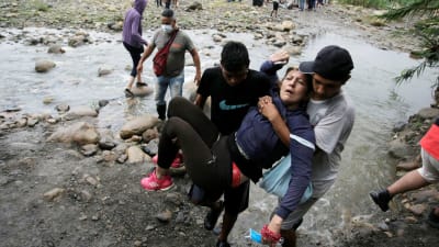 Två män bär en gammal kvinna över gränsfloden mellan Venezuela och Colombia