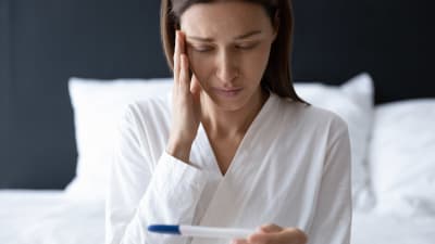 Kvinna ser på graviditetstest och håller sig för pannan