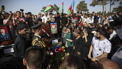 Sörjande människor står samlade kring en grav i bakgrunden syns den azeriska flaggan.