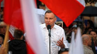 Andrzej Duda pratar in i en mikrofon vid ett talarpodium. I förgrunden syns den polska flaggan.