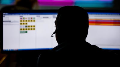 En siluett av en person som sitter framför datorn med headset på.