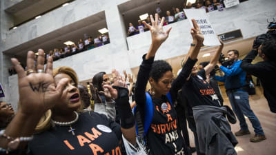 demonstranter i Hart Senate Office Building håller upp händerna. På t-skjortorna står det "I am a survivor and I vote".