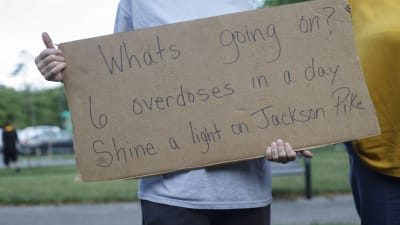En person håller en skylt under en demonstration. På skylten står "Vad är det som pågår? Sex överdoser på ett dygn."