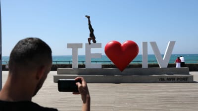 en man tar en bild på en person som stå på huvudet på en stor namnskylt där det står "te - iv" med ett hjärta i mitten.