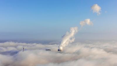 En kraftverkspipa som syns bakom vita moln.