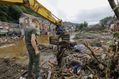 En soldat står och betraktar förödelsen i Belgien efter översvämningar. Fler personer deltar i röjningsarbetet.