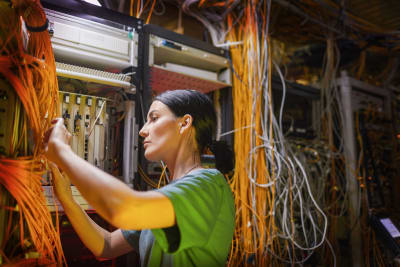 En elektriker står och jobbar vid ett elbås med en massa kablar.