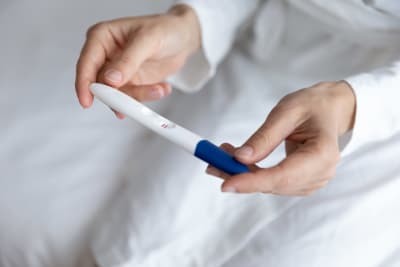 Två händer som håller i ett graviditetstest som visar två streck - alltså en graviditet.